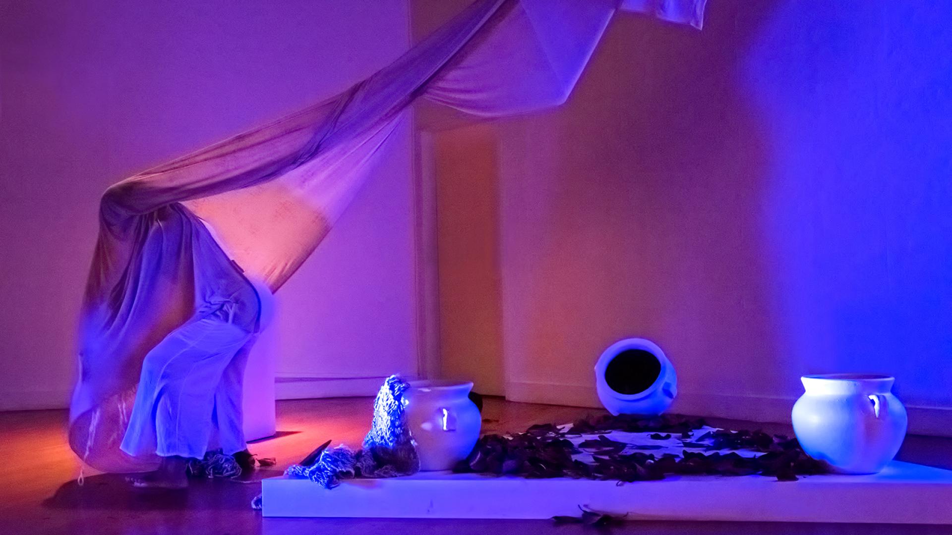 Performer beneath a sheer drape walking away from several vessels