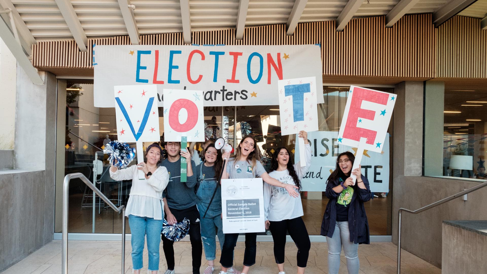 students stand in front of an Election banner holding letters VOTE 
