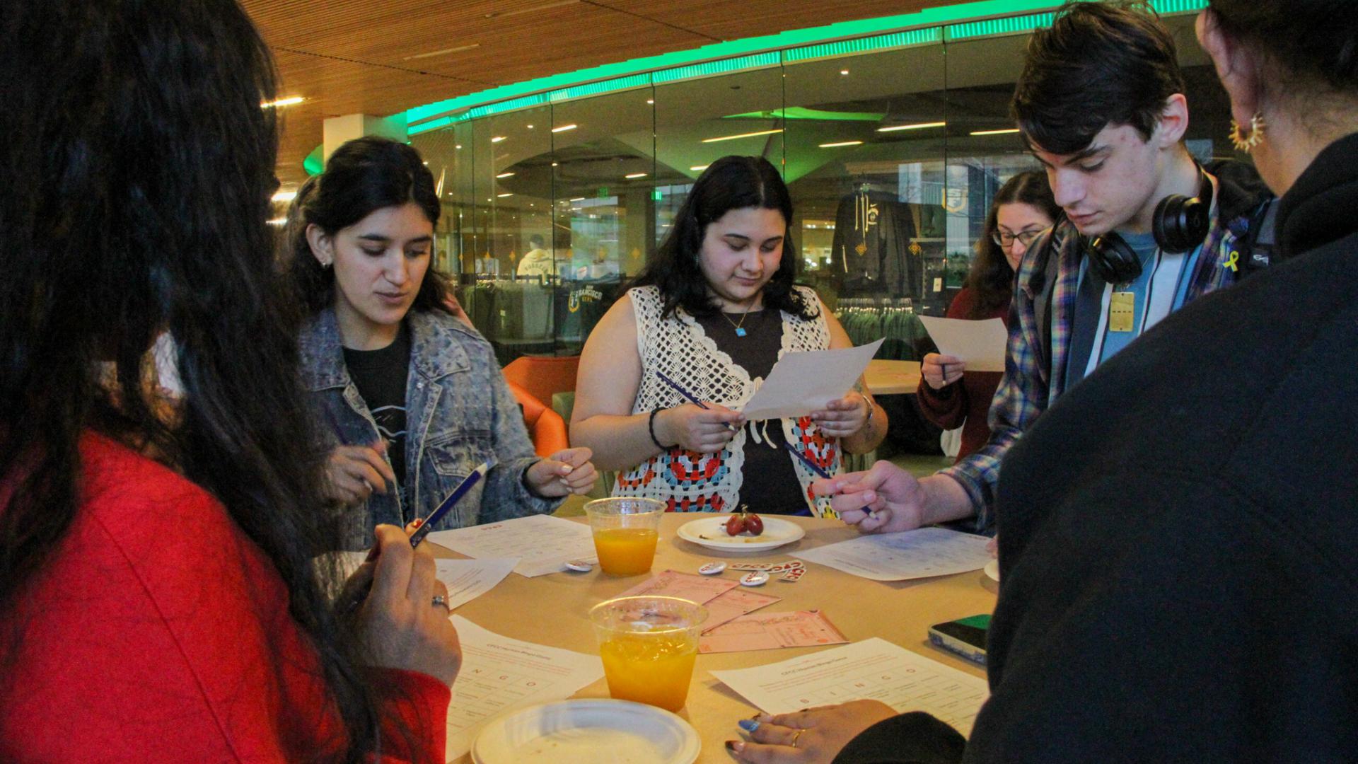 students gathered around a table with bingo sheets and beverages
