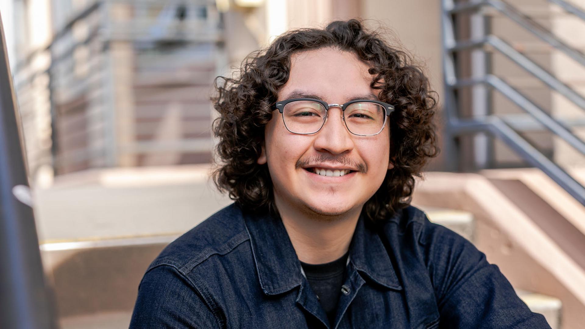 Student sits on stairs and smiles.