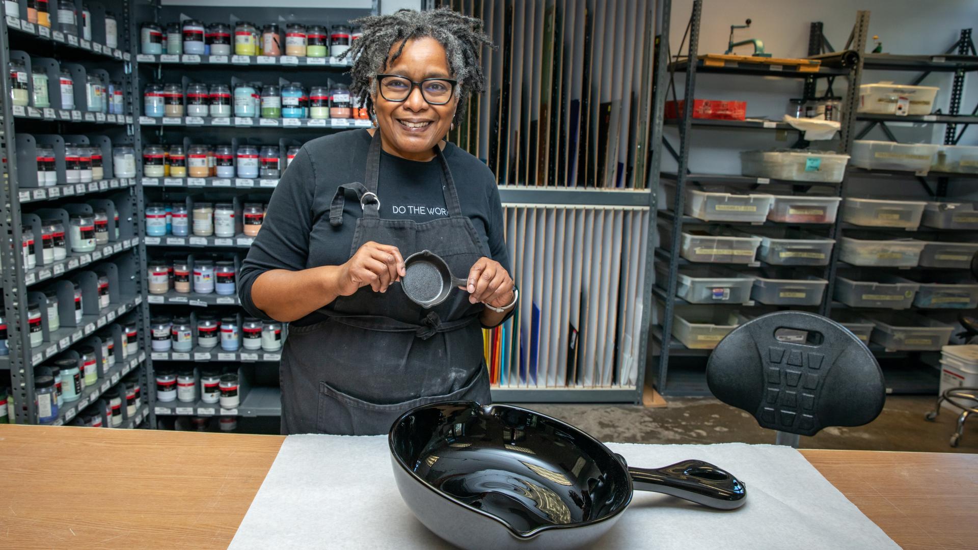 Cheryl Derricotte holding her art with art supplies behind her