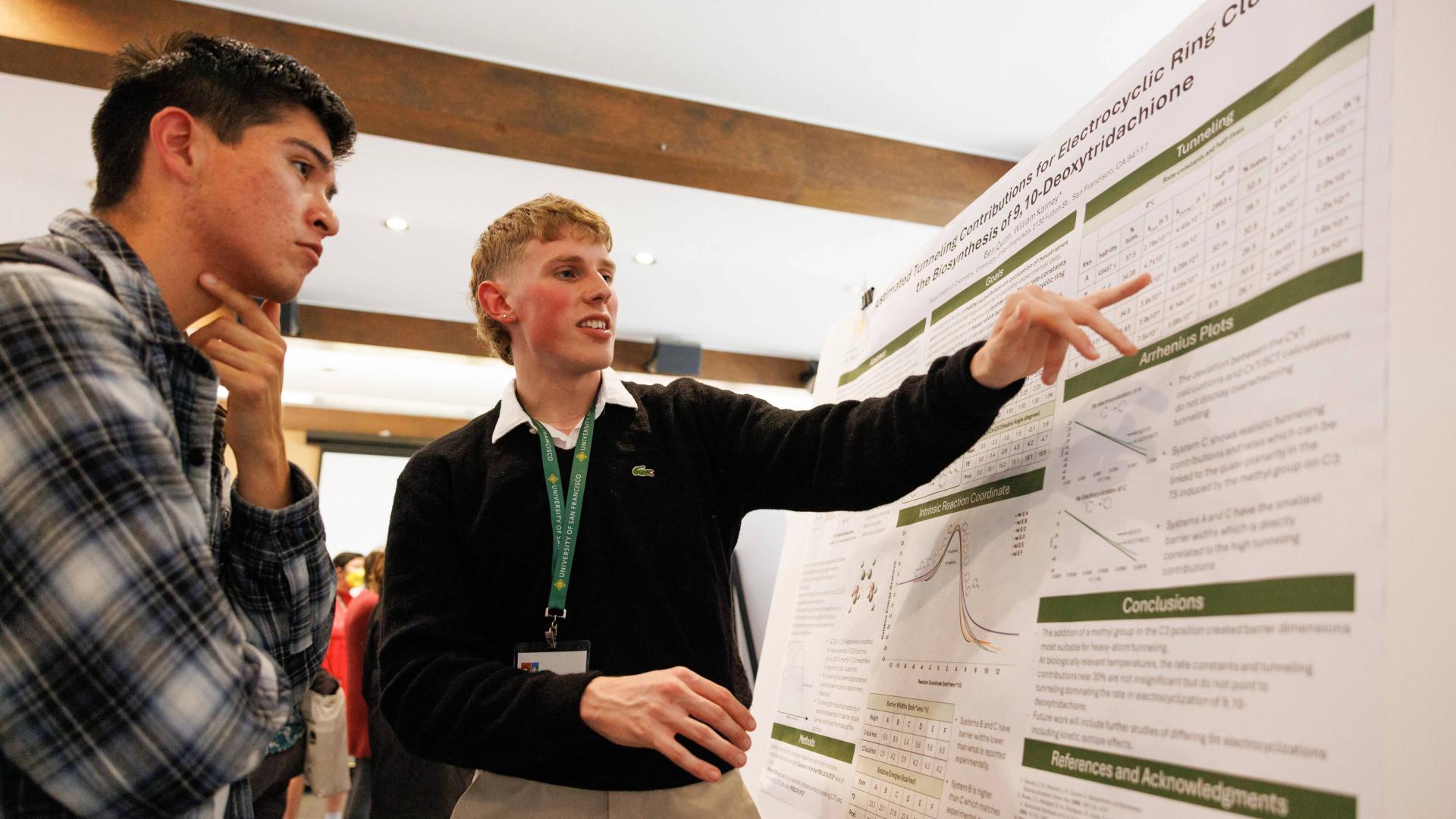Student listening to another student explain their research poster