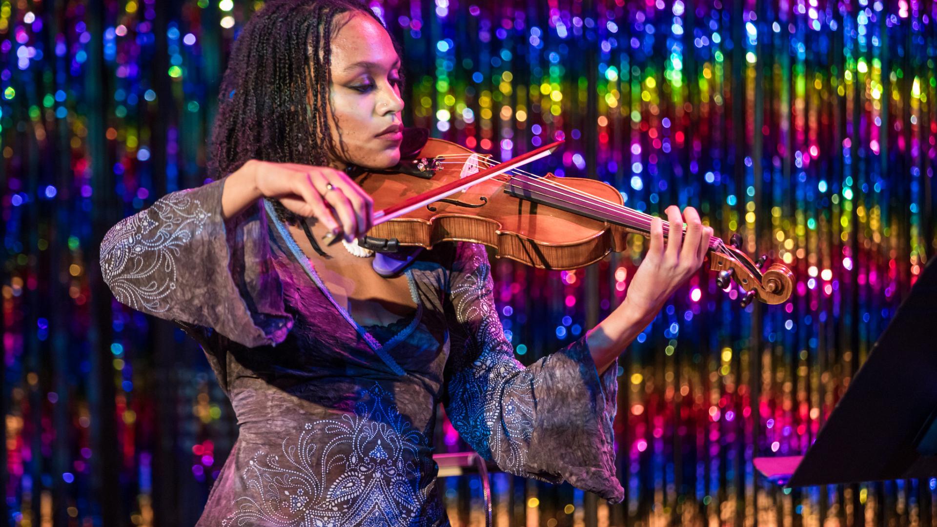 Student playing the violin against a sparkly, rainbow backdrop