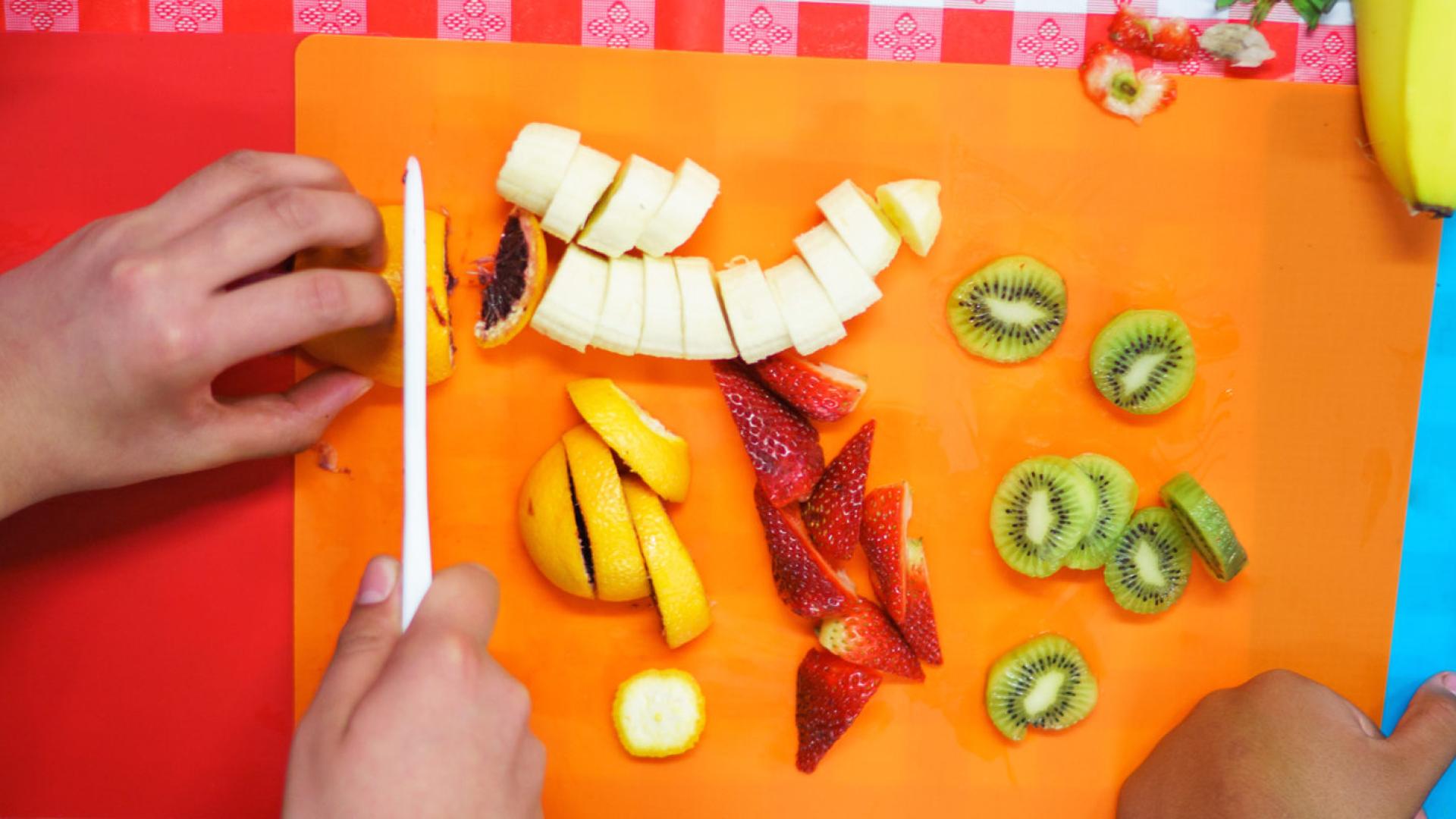 Kid chopping fruits on an orange cutting board