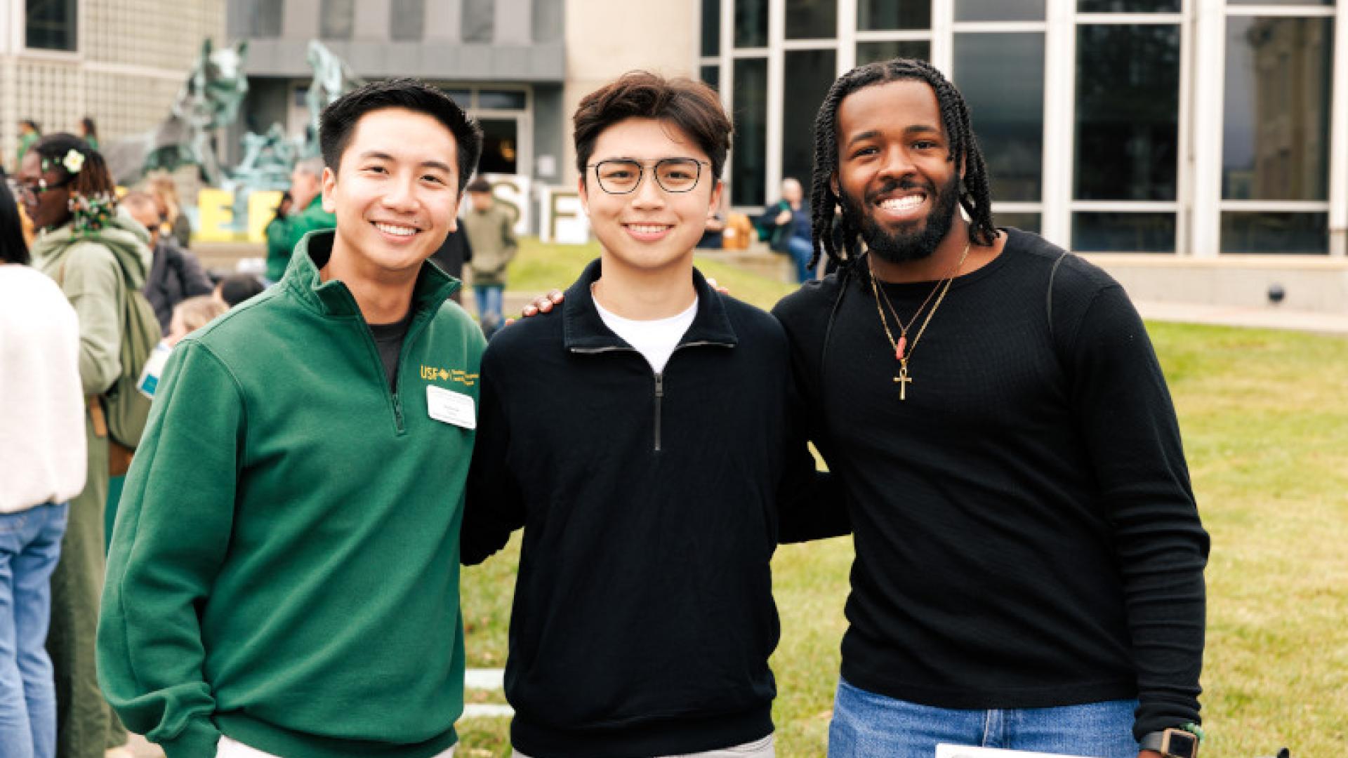 Three males students smiling at a tabling event.
