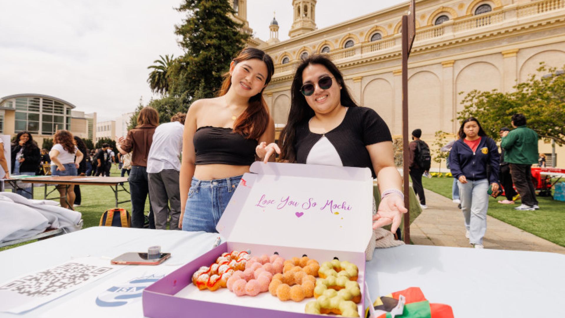 Two people giving out donuts at tabling event.