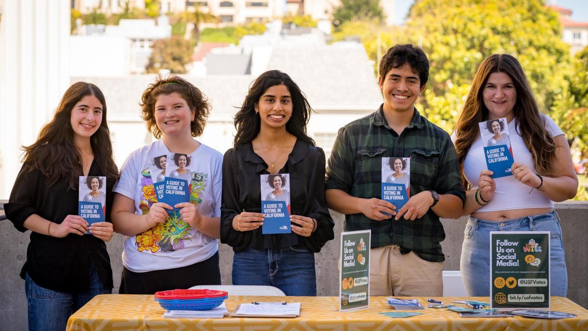 five students stand in front of a table holding voter engagement materials