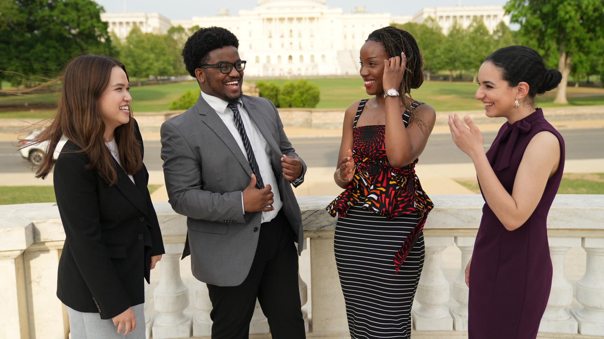 four students stand laughing with background of us capitol 